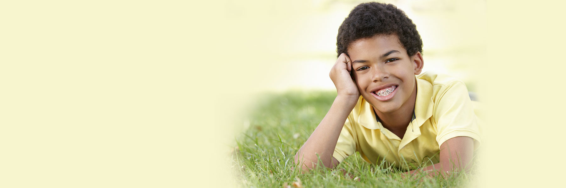 Smiling boy with braces lying on grass, illustrating braces-friendly Halloween candy tips