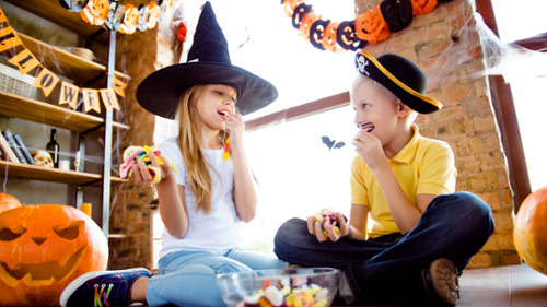 Two kids in Halloween costumes eating sugary candy surrounded by jack-o-lanterns