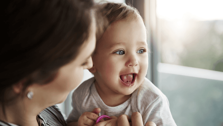 A smiling woman holds a baby, highlighting joyful infant oral care.